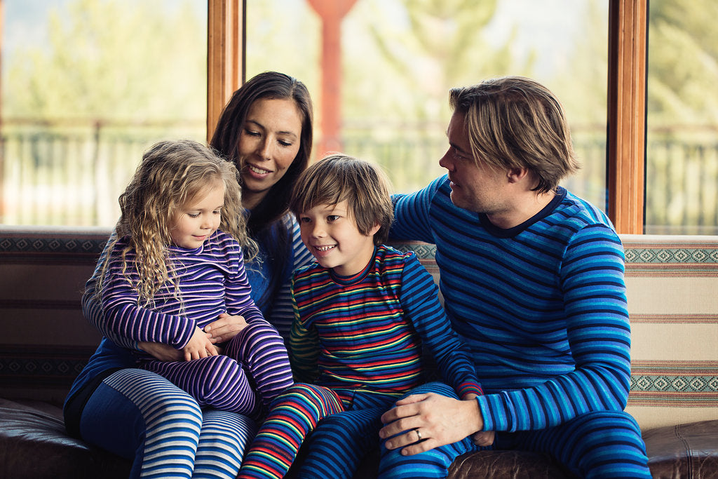 Gift Card for purchase. Family sitting on a couch wearing vibrant blue stripes, purple striped, a mixed of reds and blue striped long underwear  